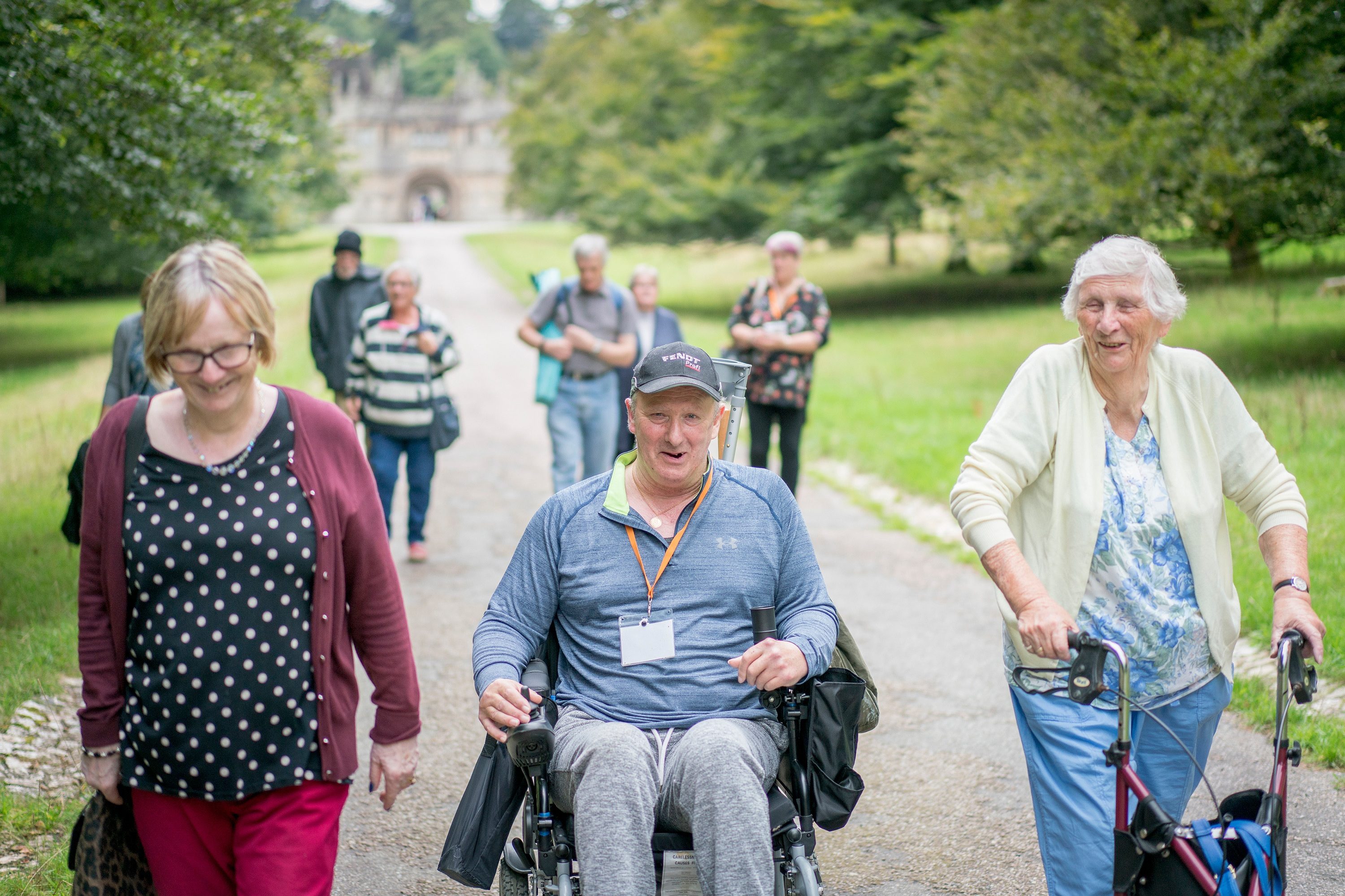 A group of older people and a man in a wheelchair walking at a National Trust property