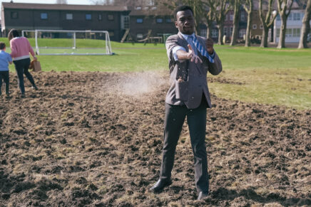A student in school uniform stands in a field and throws wildflower seed over fresh ground