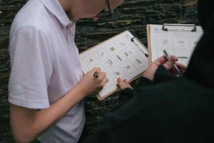 Two school students look at Widgit worksheets on clipboards