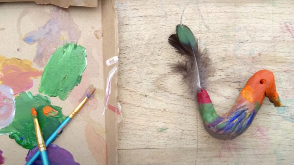 paint brushes and paint on a piece of cardboard next to a painted clay bird