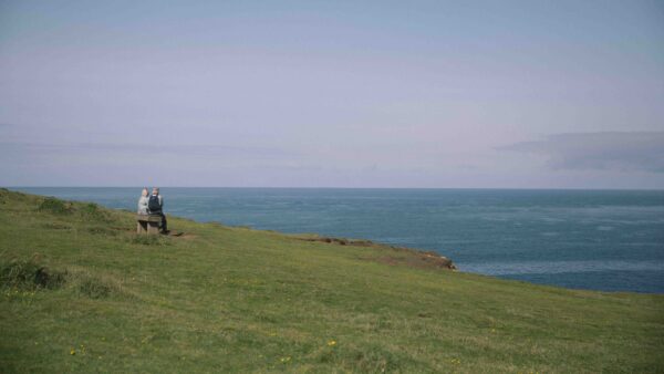 A distant view of a couple sitting on a bench looking out to sea