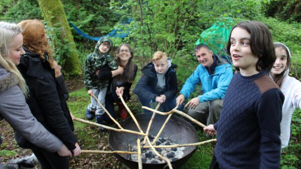A family gather around a fire to cook bread as part of a Sensory Trust activity day