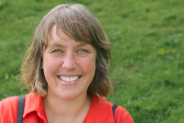 Claire Fox looks at the camera. She is outdoors with a green background behind her