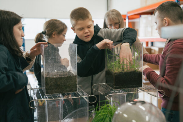 A small group of blind and partially sighted students explore two plastic tanks with their hands, one with bare soil and one with grass.