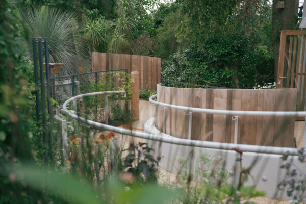 A circular path with handrail winds around a garden rich with foiliage