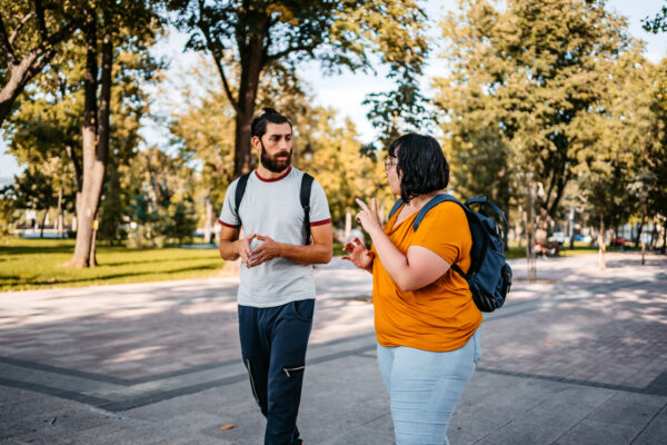 Two people walking side by side outdoors and signing to each other