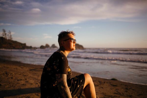 Person sits on a beach and looks out to sea. It is sunny.