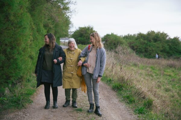 Three people are walking along a path arm in arm and laughing