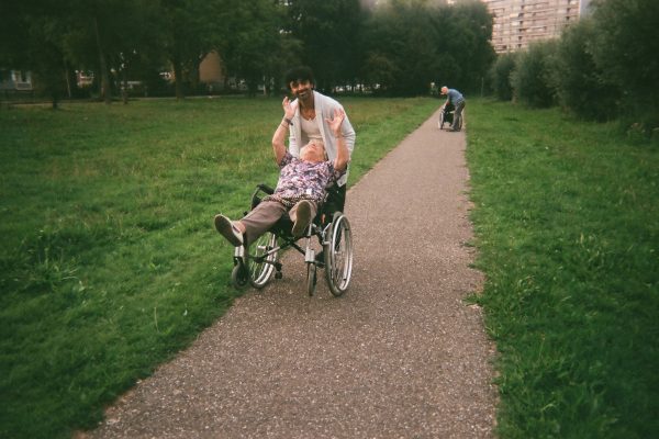 Lady in a wheelchair laughing with her hands in the air as she is being pushed along on two wheels