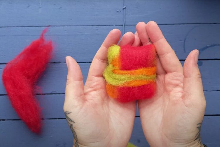 Hands with a felted soap bar inside them against a blue background