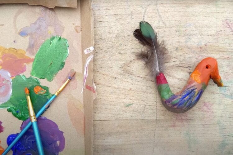 paint brushes and paint on a piece of cardboard next to a painted clay bird