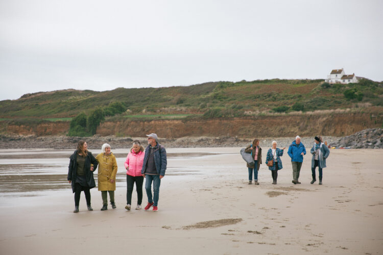 Two groups of people are walking and talking on a beach in cold weather