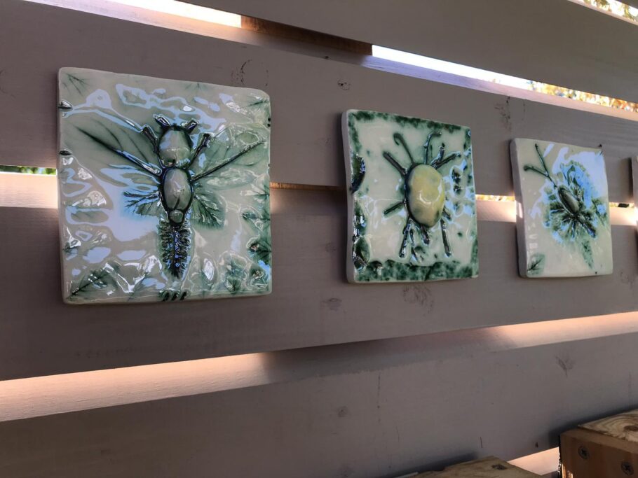 Three handmade green and cream ceramic tiles are attached to a fence